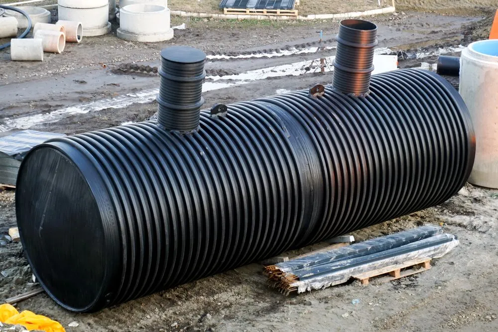 A large black corrugated plastic tank with two vertical pipe connections sits on the ground at a construction site.