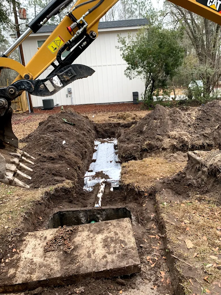 Excavator digging a trench for septic drain field pipe installation
