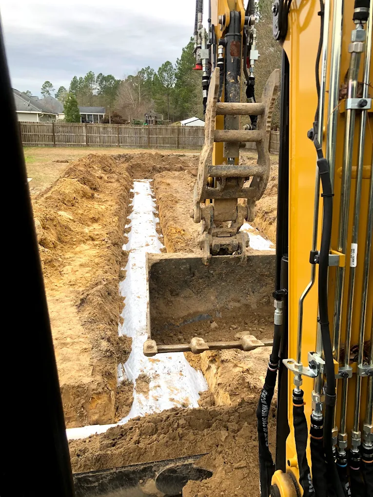 Excavator digging a septic drain field trench with distribution pipe